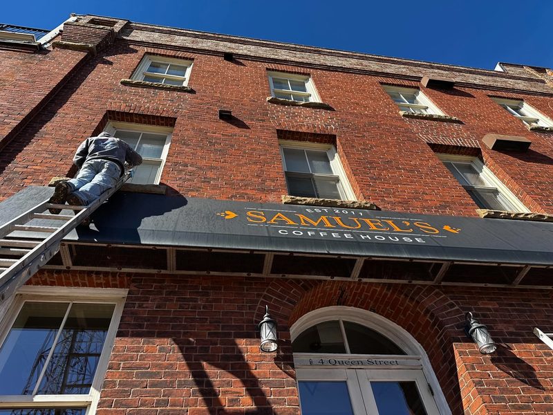 A worker on a ladder at second-storey level of a red brick commercial building in downtown Charlottetown, working on the awning frame