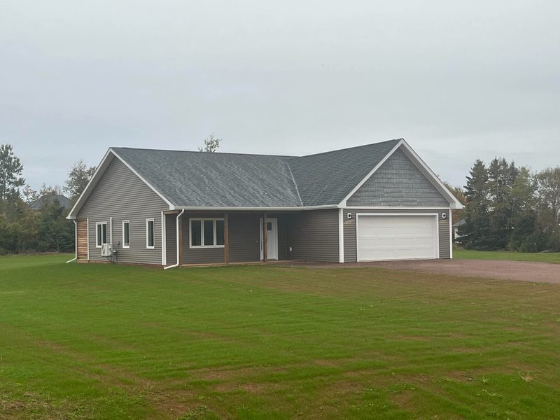 A grey ranch bungalow with a gabled entry, dormers and an attached garage on a green lawn