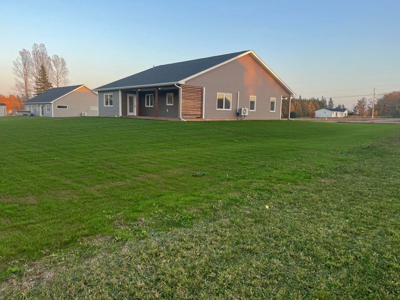 The same grey ranch bungalow across a wide lawn with autumn trees behind