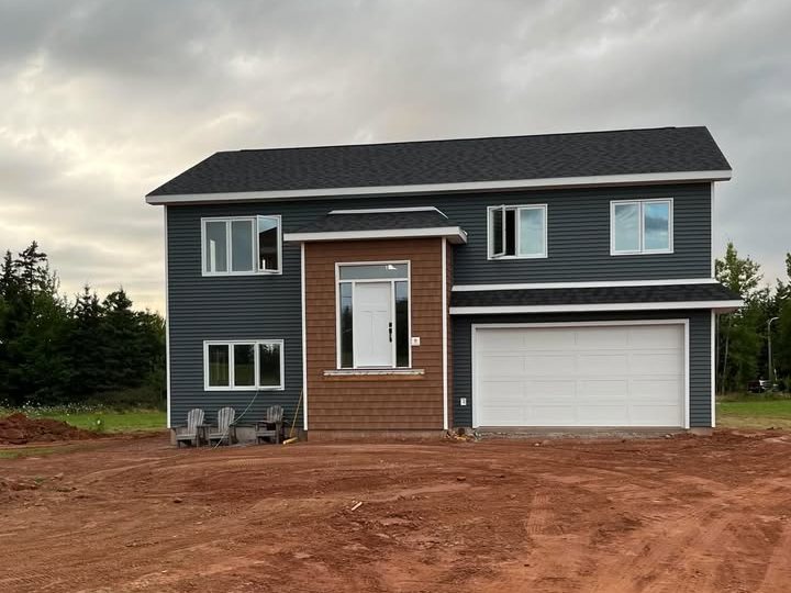 A navy two-storey house with a shingled entry bay and double garage on a freshly graded red-soil lot under a grey sky