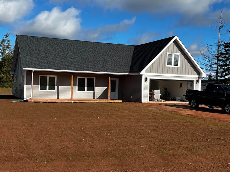 A finished white board-and-batten farmhouse with a covered porch and double garage on a red-soil lot