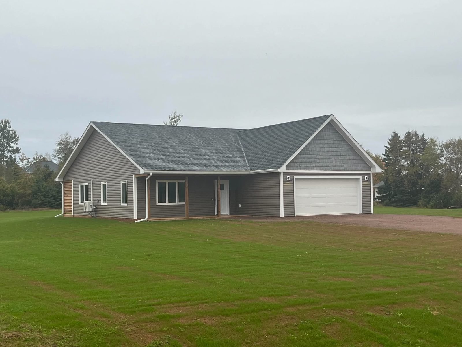 A finished grey ranch bungalow with a gabled entry, dormers and an attached garage on a green lawn