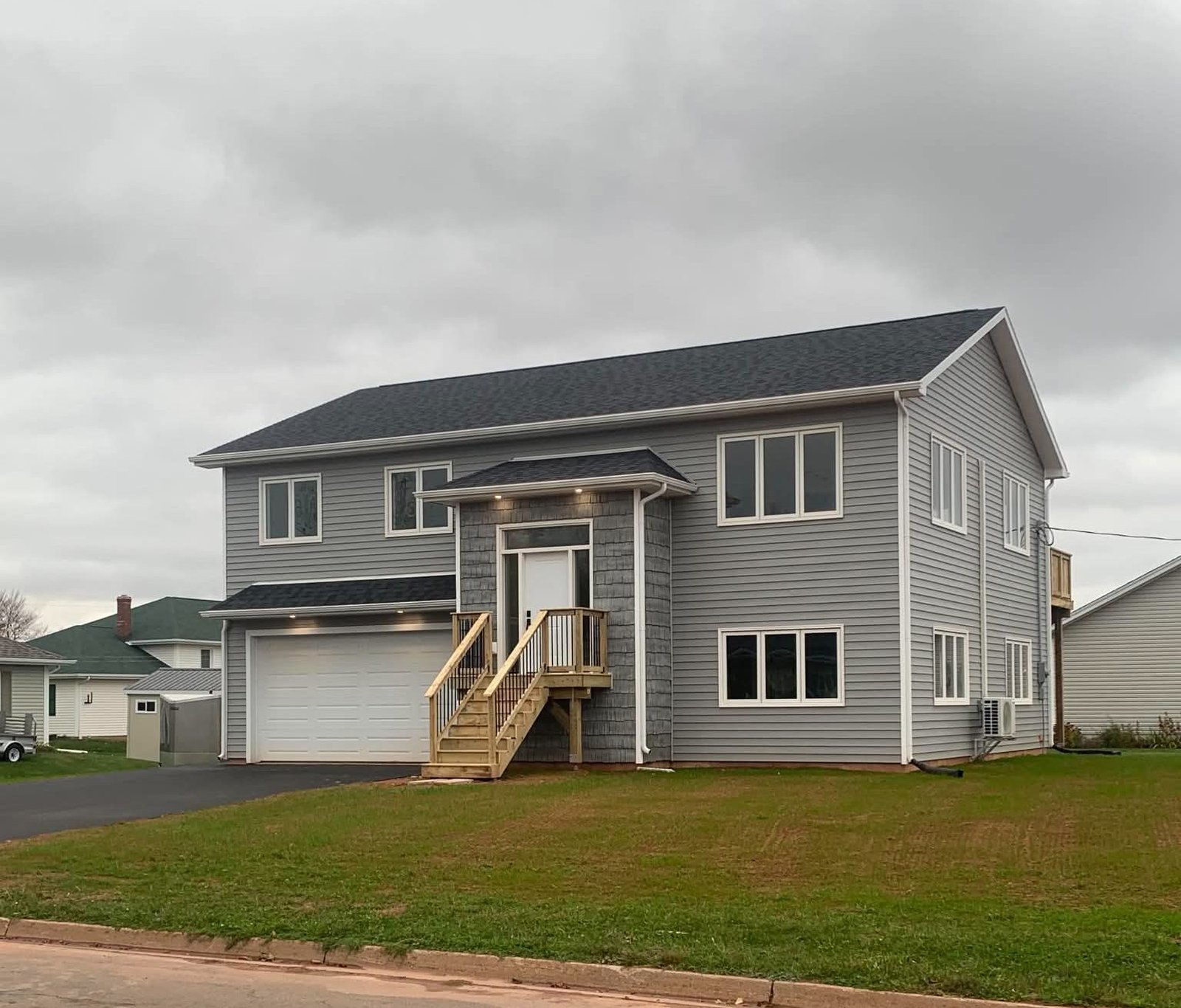 A finished grey split-entry home with wooden front steps and an attached garage