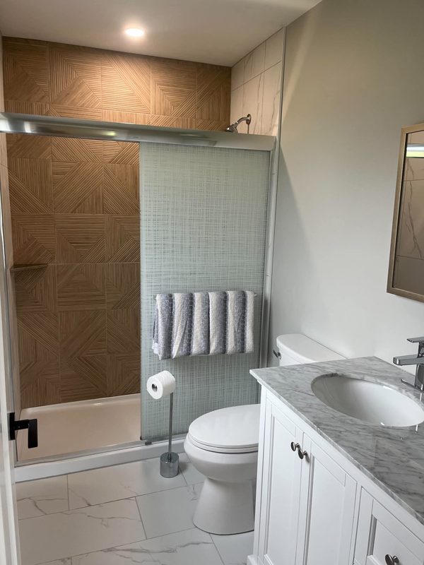 A bathroom with a patterned wood-look feature wall inside a glass-screened shower and a marble-counter vanity