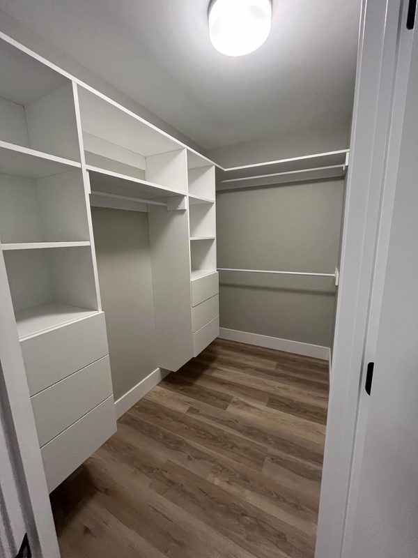 An empty walk-in closet with white built-in shelving, hanging rails and a drawer bank