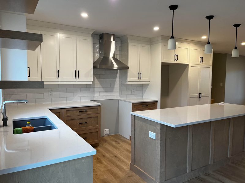 A kitchen with white uppers, a grey and wood island, subway tile and quartz counters