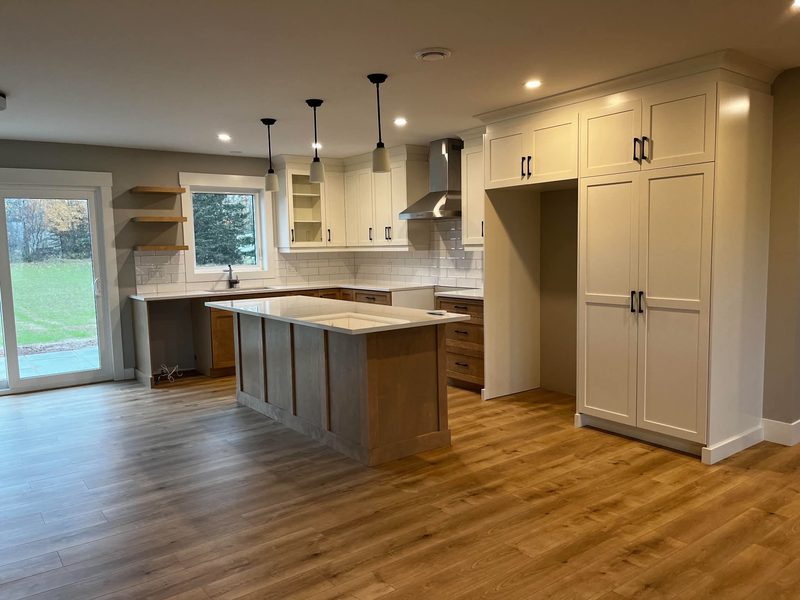 A kitchen with white shaker uppers, wood lowers, a large island and three pendants